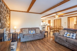 Ein gemütliches Wohnzimmer mit Steinwand, Holzbalken, Kamin und Essbereich mit Holzmöbeln.