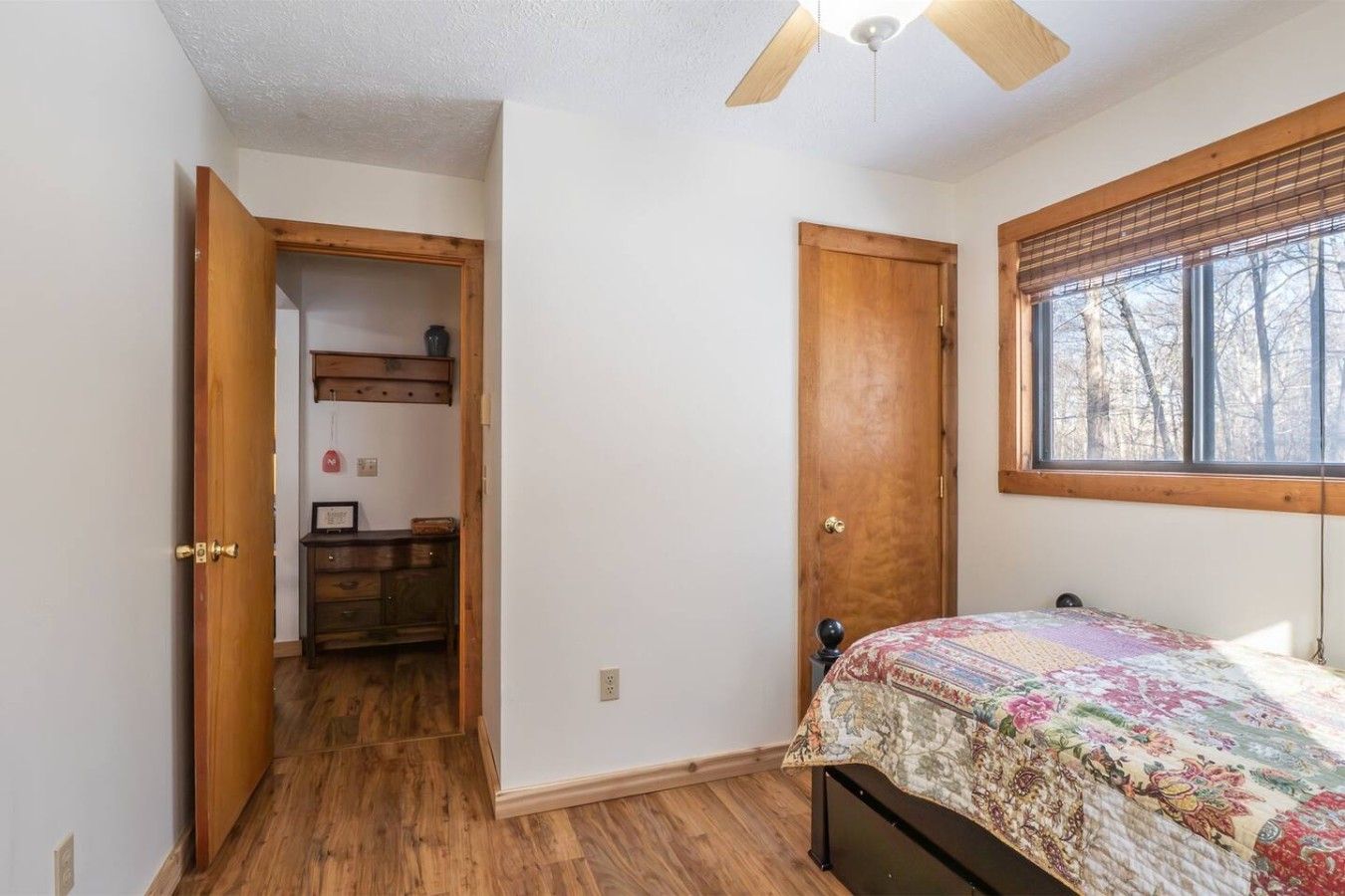 Un dormitorio con cama de madera, una ventana con persianas, una puerta y un ventilador de techo.