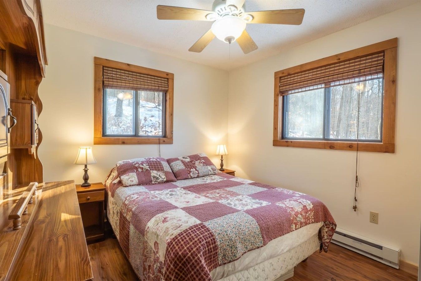 Un dormitorio con una cama de madera, dos lámparas de noche, un ventilador de techo y dos ventanas con persianas.