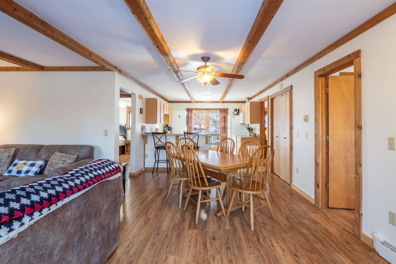 A cozy living room with a sofa, a patterned throw, and a dining area with wooden chairs and a table.
