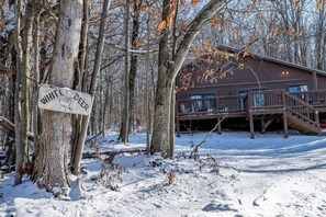Uma cabana com varanda e placa indicando 'WHITE DEER' em um cenário florestal nevado.