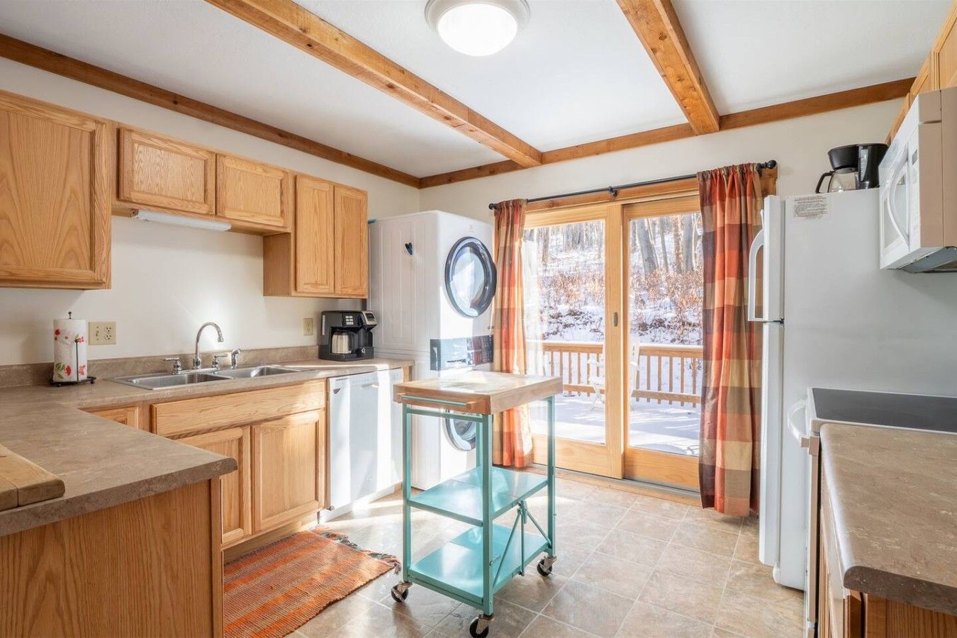 A kitchen with wooden cabinets, a sink, a coffee maker, and a glass cart.