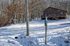 A cabin with a deck and a signpost in a snowy forest.