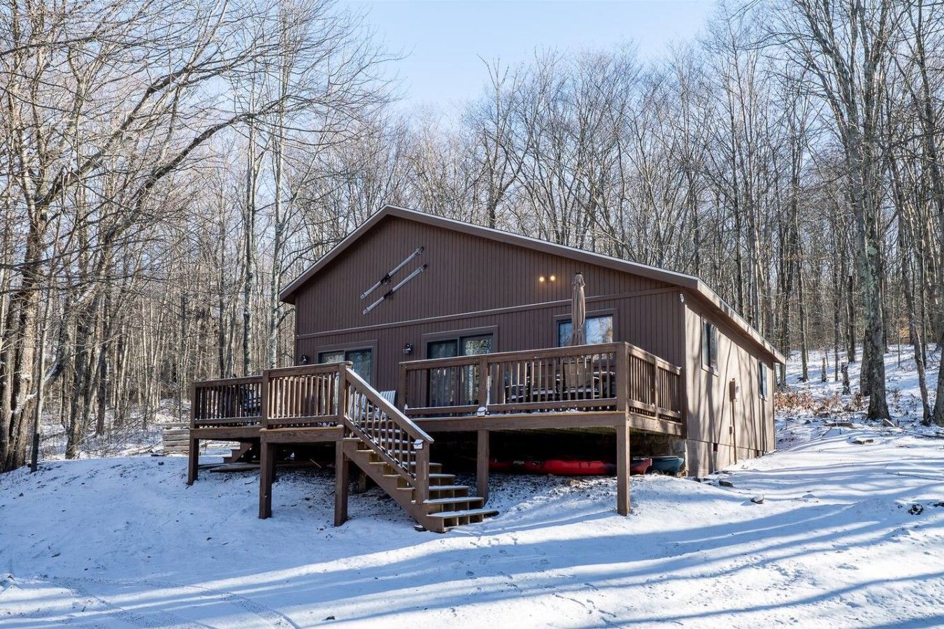 Une cabane en bois dotée d’une terrasse, entourée d’arbres et de neige.