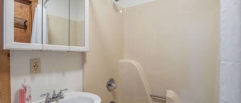 Un baño con lavamanos blanco, espejo, ducha con puerta de cristal y puerta de madera.