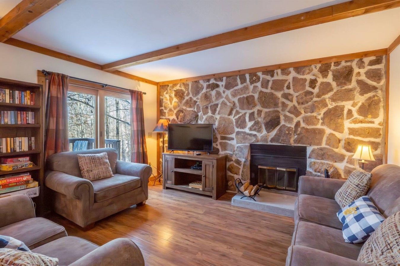 A cozy living room with a stone wall, fireplace, and wooden beams.