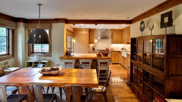Een ruime keuken met houten kastjes, een centraal kookeiland en een eethoek met metalen stoelen.