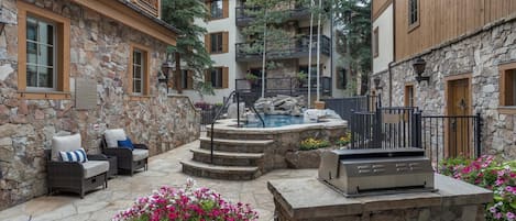 A courtyard with a stone barbecue, outdoor seating, and a hot tub.