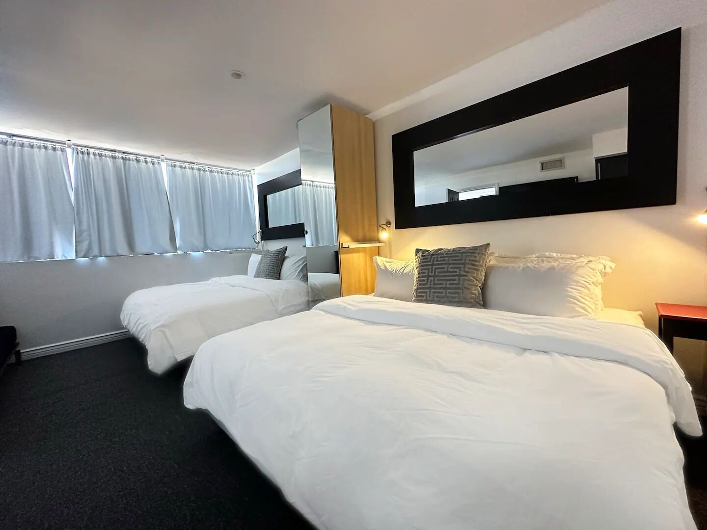 A hotel room with two beds, a large mirror, and a window with curtains.