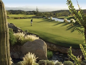 Een golfbaan met een persoon in spel, omringd door cactussen en rotsen.