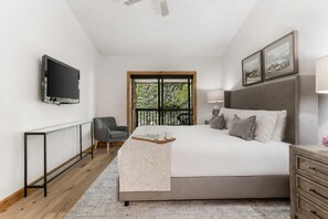 Een slaapkamer met een bed, nachtkastje, stoel, televisie, raam en kunstwerk.