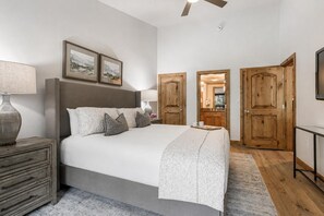 Een slaapkamer met een groot bed, houten deuren, een plafondventilator en ingelijste foto’s aan de muur.