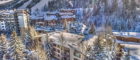 Un complejo turístico nevado con varios edificios, incluyendo una cabaña y un hotel, rodeado de árboles y una pista de esquí.