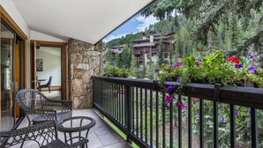 A balcony with wicker furniture, stone walls, and a view of a mountain resort. - Riva Ridge Premium 745 | 2BR Vail Village (Vail)