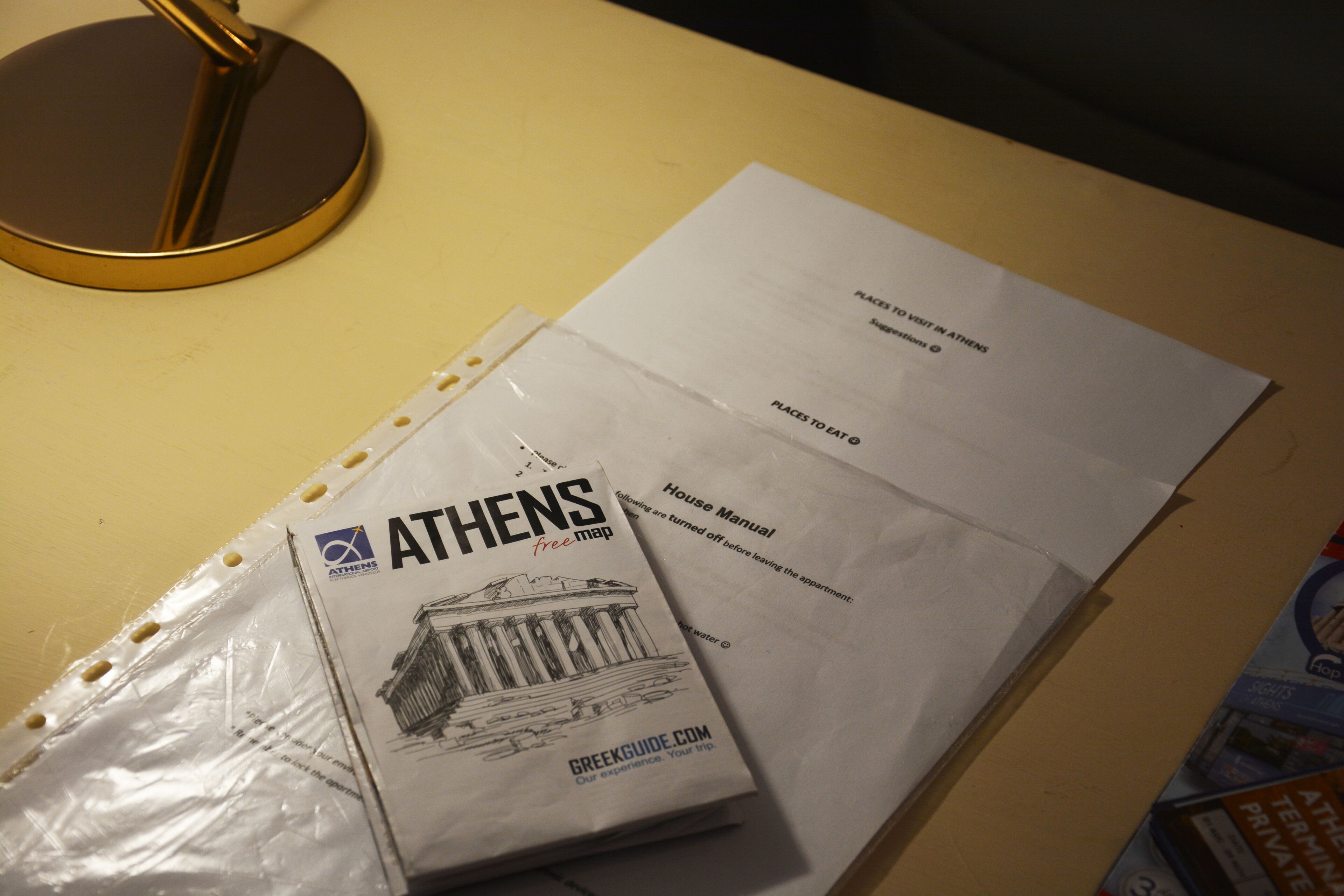 A desk with a map of Athens, a House Manual, and a plastic-wrapped item.