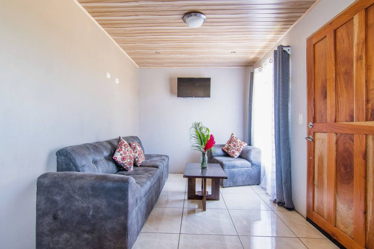 Un salon moderne avec deux canapés gris, une table basse en bois et un téléviseur fixé au mur.