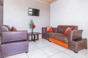 A living room with a brown leather sofa, a matching armchair, and a small wooden table with a vase of flowers. - Casa Monarca (Monteverde)