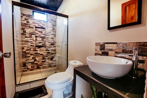 A bathroom with a glass-enclosed shower, a white toilet, and a large white sink with a marble countertop. - Casa Monarca (Monteverde)