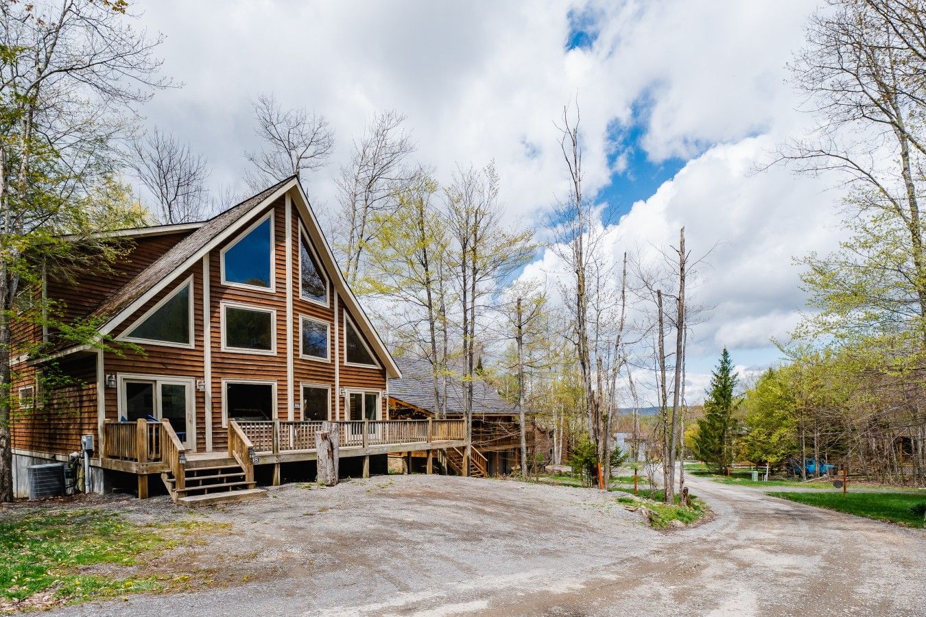 A wooden cabin with a porch and a gravel driveway.