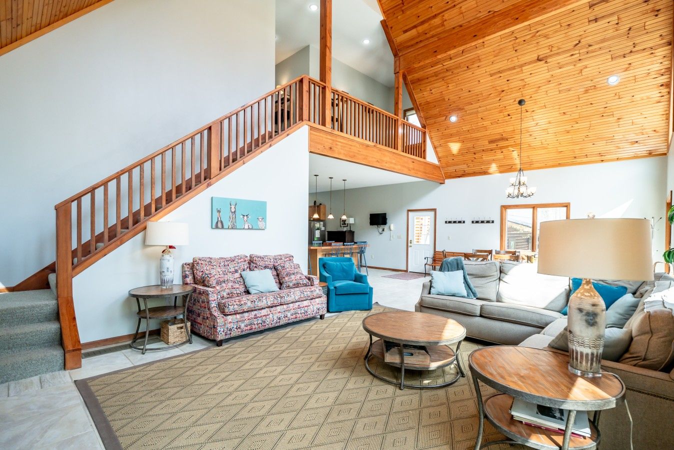A spacious living area with a wooden staircase, a patterned sofa, a blue armchair, and a grey sofa.