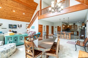 A spacious living area with a high ceiling, wooden beams, a dining table, and a kitchen area.