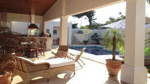 An outdoor patio with wicker furniture, a pool, and a potted plant. - SINGLE STOREY HOUSE - COMFORT AND LEISURE - ENSEADA - GUARUJÁ - (Guarujá)