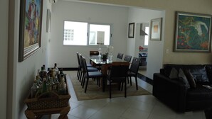 A dining area with a table and chairs, a black leather sofa, and a wall with framed artwork. - SINGLE STOREY HOUSE - COMFORT AND LEISURE - ENSEADA - GUARUJÁ - (Guarujá)