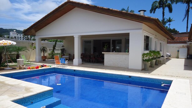 A residential pool area with a covered patio, lounge chairs, and a clear blue pool. - SINGLE STOREY HOUSE - COMFORT AND LEISURE - ENSEADA - GUARUJÁ - (Guarujá)