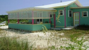 A single-story house with a covered porch, a small front yard, and a sandy beach in the background. - Secluded beach house on Hooper's Bay, Great Exuma, The Bahamas (George Town)
