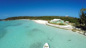 A coastal resort with a clear turquoise sea, a white sandy beach, and a small building with a green roof.