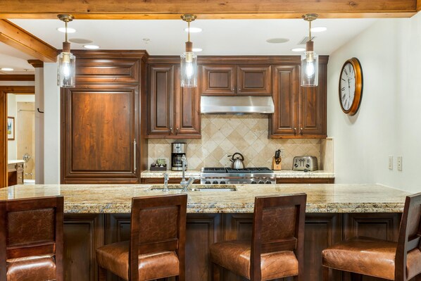 Una cocina con armarios de madera, encimera de granito, campana extractora de acero inoxidable y una barra con sillas.