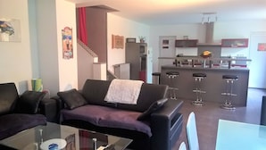 A modern living room with a glass coffee table, a sofa, and a kitchen area with a bar and stools. - Beaucaire Avignon, Camargue  (Beaucaire)