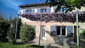 A two-story building with a balcony covered in purple flowers, a door, and a small outdoor seating area with a table and chairs. - Beaucaire Avignon, Camargue  (Beaucaire)