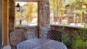 Un patio techado con una pared de piedra, una mesa redonda y sillas de mimbre.