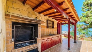 Cucina esterna con parete in pietra, piano di lavoro in legno e pensili rossi.
