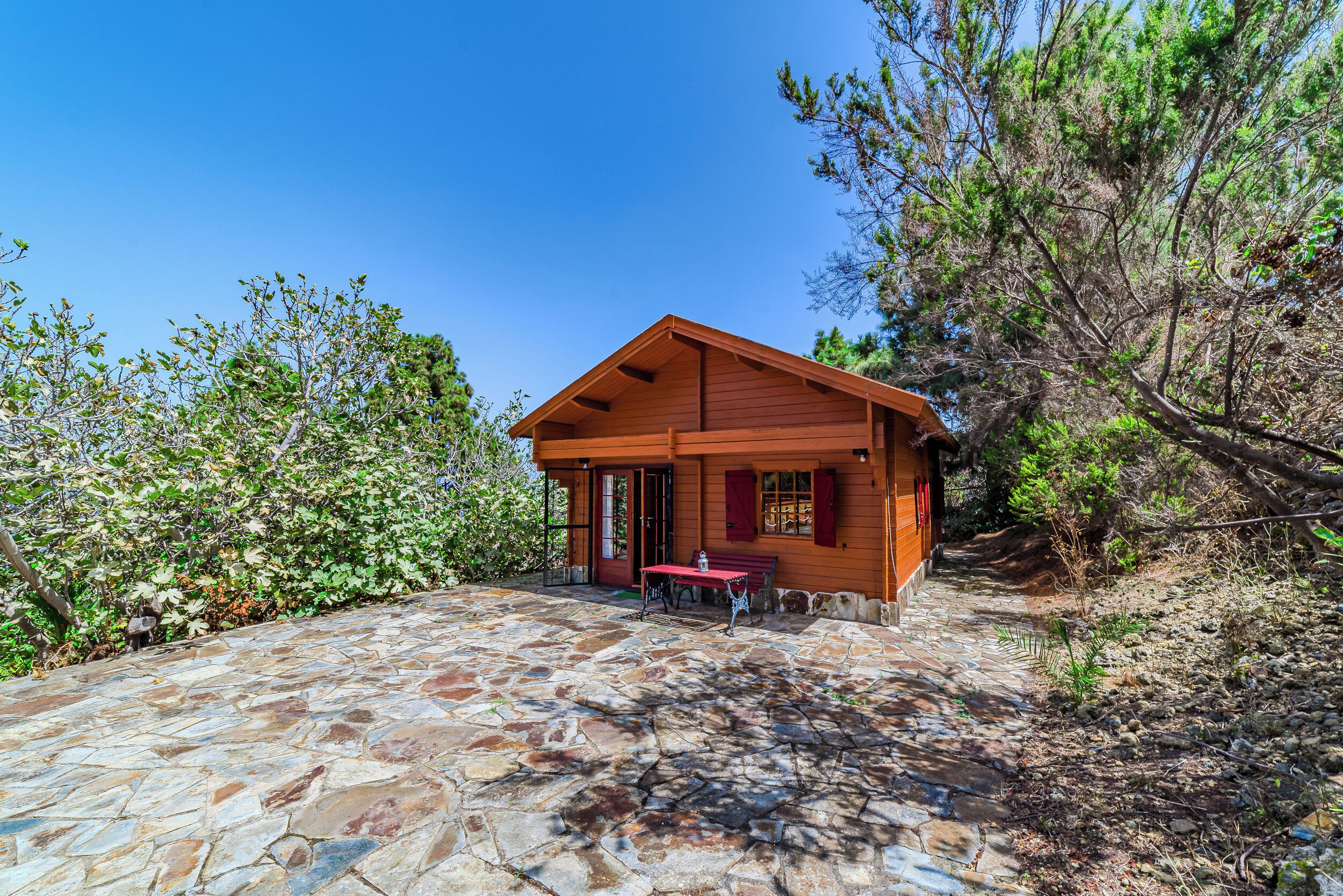 A wooden cabin with a stone patio, surrounded by trees.