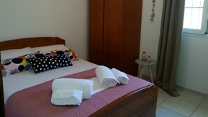 Une chambre d’hôtel avec un lit, une armoire, une petite table avec des bouteilles et une fenêtre avec des rideaux.