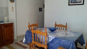 Un coin repas avec une table recouverte d’une nappe bleue, des chaises en bois, un bol bleu et un tableau encadré accroché au mur.