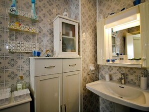 Um banheiro com azulejos estampados, um armário branco com gavetas, uma pia e um espelho.