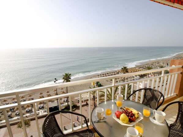 A balcony with a table set for breakfast overlooking a beach.