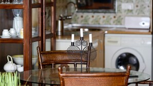 A dining area with a glass table and wicker chairs, a cabinet with glassware, and a microwave in the background. - SUITUR APARTMENT YATE BEACHFRONT FUENGIROLA (Fuengirola)