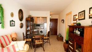 A cozy living room with a dining area, a kitchen in the background, and a wooden cabinet with drawers. - SUITUR APARTMENT YATE BEACHFRONT FUENGIROLA (Fuengirola)