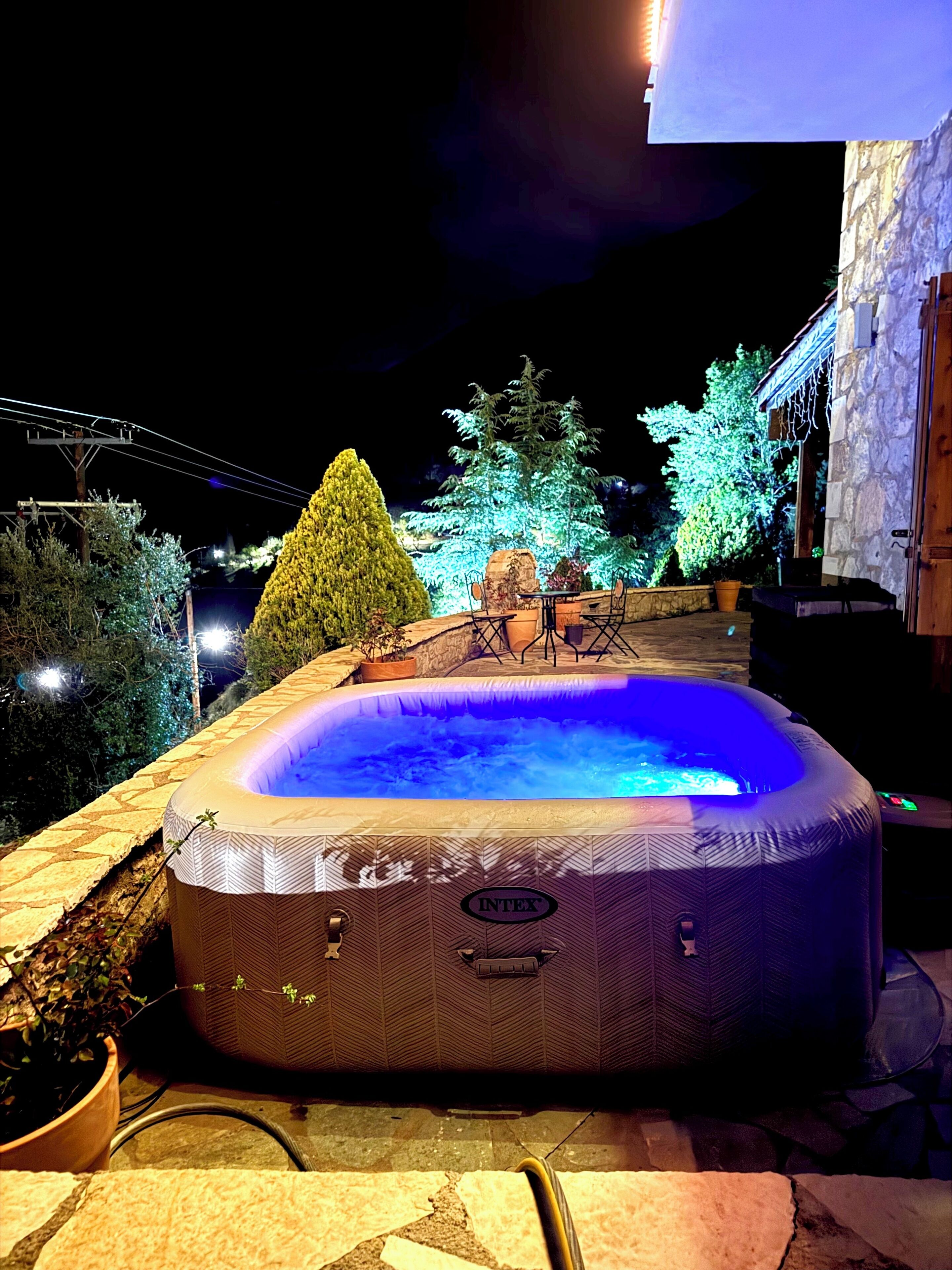 An outdoor hot tub with a stone surround, surrounded by potted plants and trees.