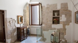 Ein Zimmer mit Stehwänden, einem Holzschrank, einem Korbstuhl, einer Glastausche und einem Fenster mit Blick.