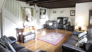 A living room with a staircase, leather sofas, a TV, and a wooden floor.