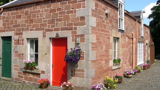 A stone building with a red door, multiple windows, and flower boxes on the ground.