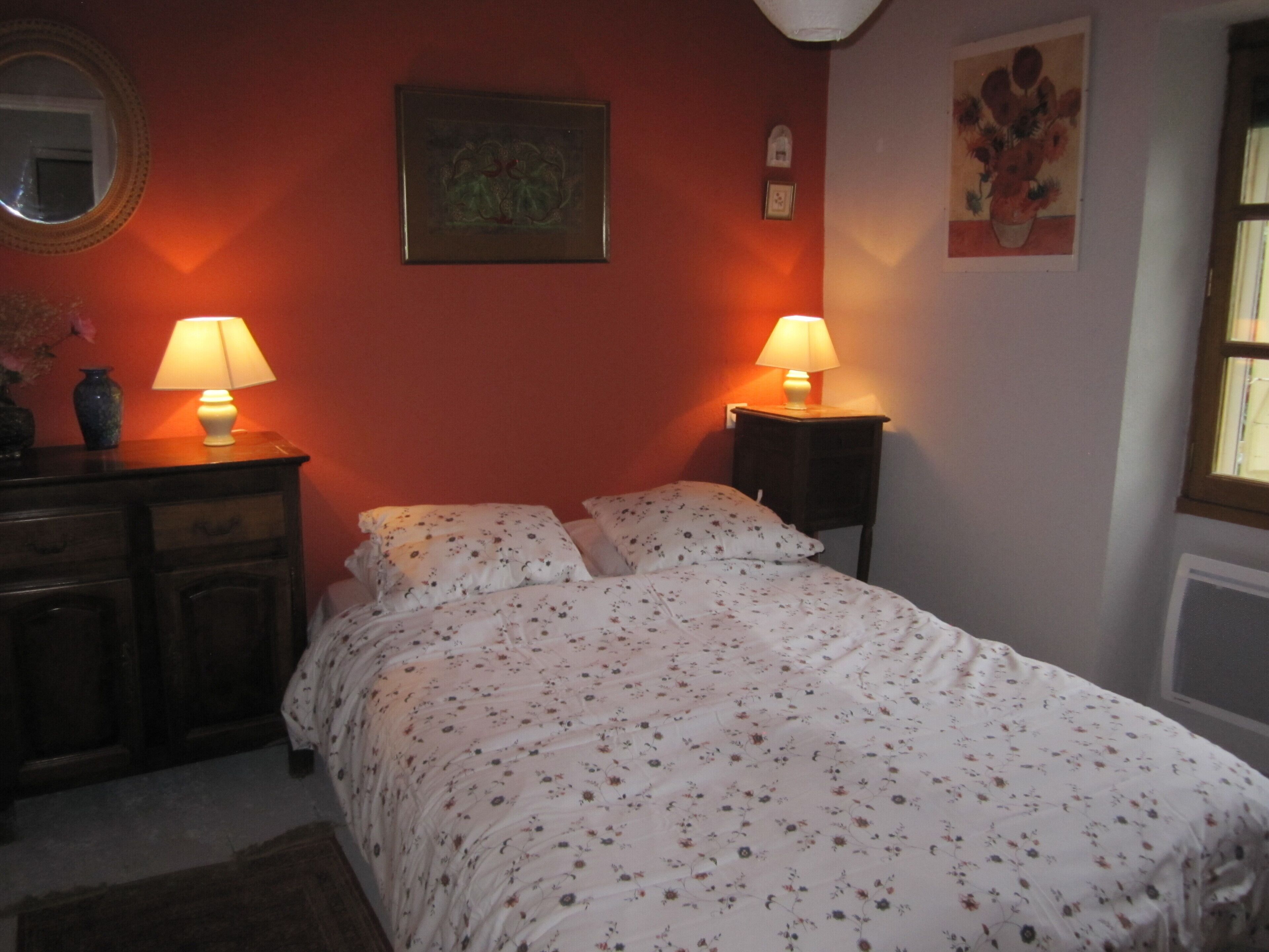Ein Schlafzimmer mit einem Bett, zwei Nachttischlampen, einem Schminktisch und einem Spiegel, sowie einem Gemälde an der Wand.