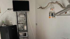Um espaço de estar compacto com um sofá branco, uma geladeira preta, um micro-ondas e uma TV na parede.