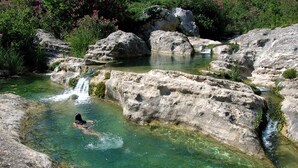 Uma piscina natural com água límpida, rodeada por grandes rochas e vegetação exuberante.
