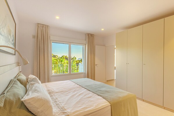 A bedroom with a large bed, a wardrobe, and a window with a view of greenery. - Villa Mar Alborán, Great Seaviews, 5-10 Min Easy Stroll Town & Beaches (Moraira)